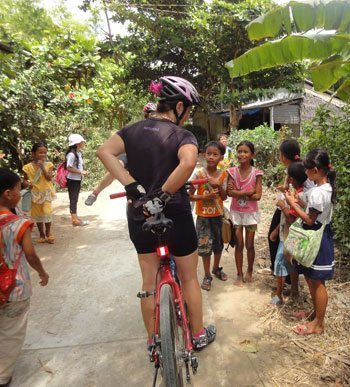A cyclist greeted warmly by young Cambodian children.