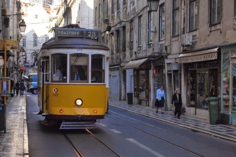 A yellow trolley chugs up a narrow Lisbon street.