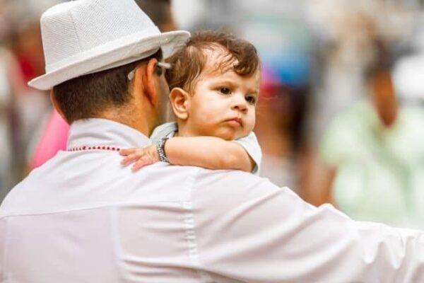A toddler clinging to his fathers shoulder on the streets of Central Havana. Branson Quenzer Photos.