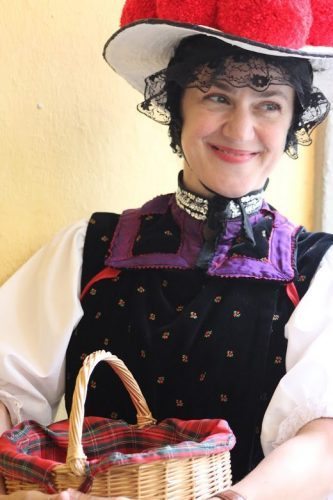 Wearing a Bollenhut hat adorned with cherry-red pom-poms, Nicole Djandji, a delightful Freiberg city tour guide looks, fetching in her traditional Black Forest costume once worn by unmarried girls.