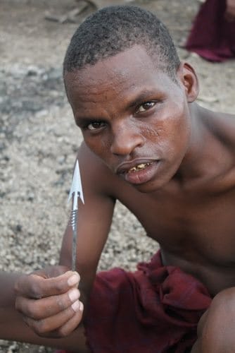 A blacksmith shows his work and his tribal scars on his face. 