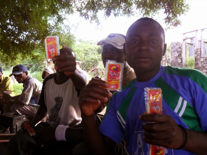 Young men idle away the afternoon under a tree drinking sachets of alcoholic spirits, listening to the radio and playing cards.
