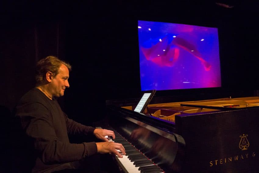 The pianist Christopher O'Riley plays as the puppet show ensues behind him.