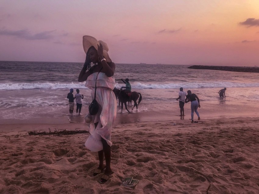 My cousin grabbing to her hat as the tide tosses her into a fanciful pose on the West Africa coast..