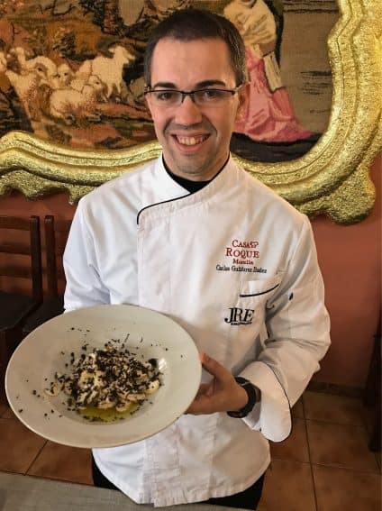Chef Carlos Gutierrez Ibáñez of Casa Roque in Morella, smiles while holding a traditional delicacy, fresh picked white mushrooms sprinkled with lemon juice and black truffles.