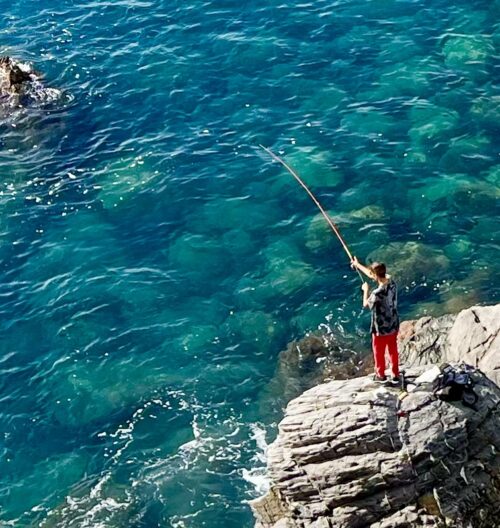 fisherman balancing act in the crystal clear waters below Castel Dragone.