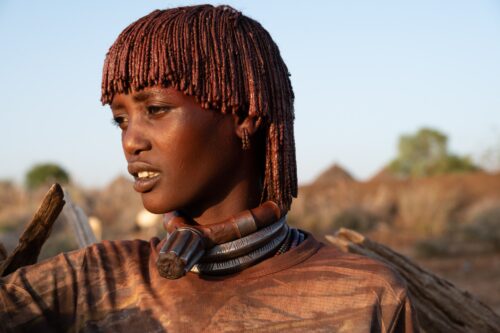 Hamar women use a mixture of butter and ochre powder to coat their hair and twist it into dreadlocks. The thick copper necklace indicates she is the first wife.
